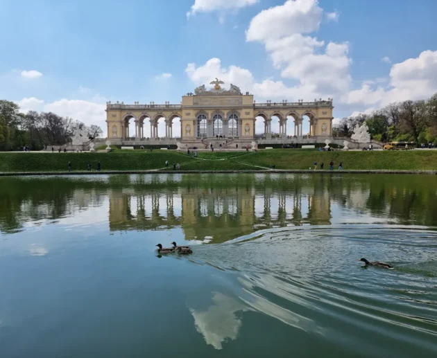 Schloss Schönbrunn reflected in water, with ducks swimming; Vienna landmark.