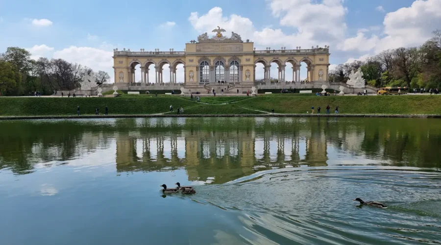 Schloss Schönbrunn reflected in water, with ducks swimming; Vienna landmark.
