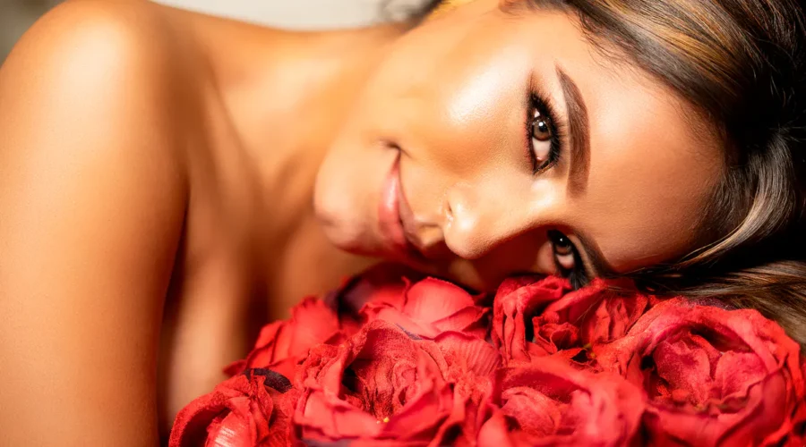 Lächelnde Frau mit strahlender Haut, ruhend auf roten Rosen