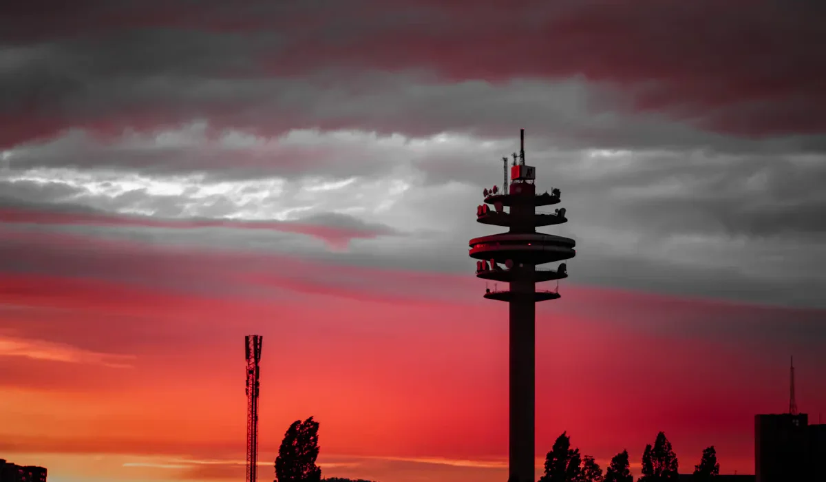 Silhouette of telecommunications towers against a fiery red sunset sky.