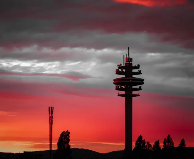 Silhouette of telecommunications towers against a fiery red sunset sky.