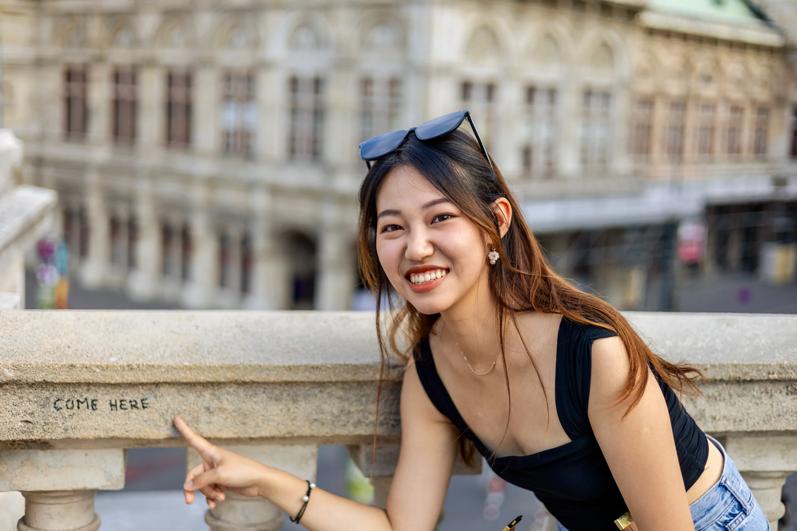 Lächelnde Frau vor Wiener Gebäude mit Sonnenbrille auf dem Kopf.