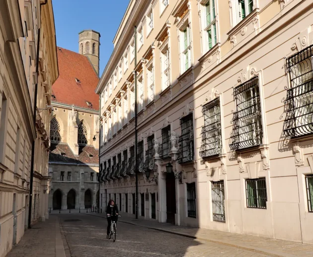 Cyclist on quiet Vienna street with historic buildings, possibly near a Hydrafacial spot.