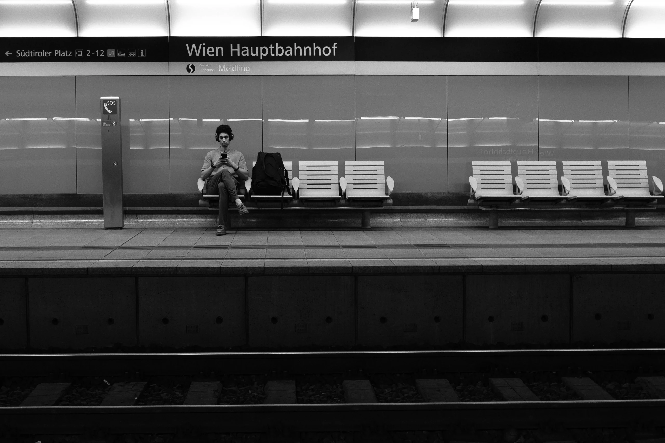 Black and white photo of man waiting at Wien Hauptbahnhof train platform.