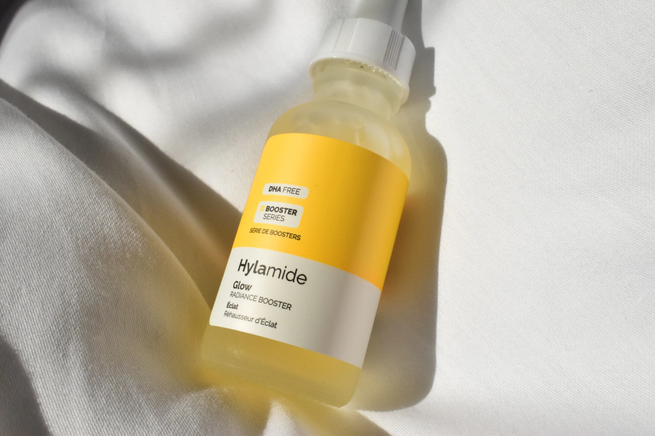 Nahaufnahme einer Hylamide Glow Radiance Booster Flasche auf weißem Stoff.